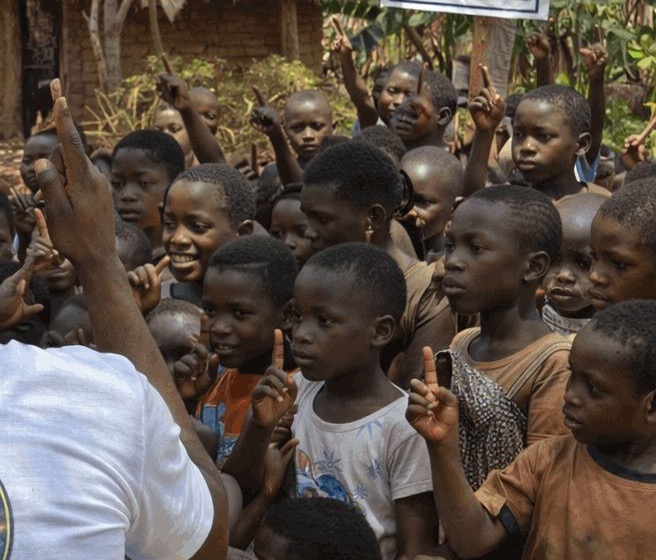 A crowd of smiling children with their hands raised at a village school